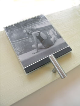 3. Align the top edge of the jewel case to the top edge of the board and press firmly into place. Drill a hole for a handle, knob, or hook to hang the towel under each photo. Mount the towel rack to your bathroom wall with screws at each end.